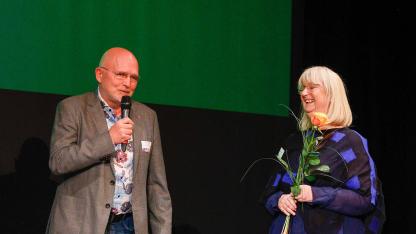 Mann mit Mikro und Frau mit Rose in der Hand stehen auf einer Bühne